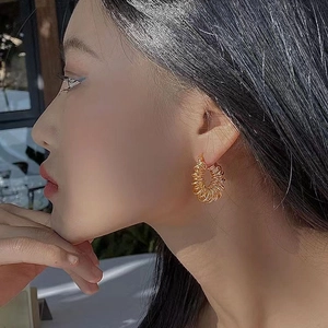 Close-up of a female model wearing stylish golden twisted hoop earrings in natural light