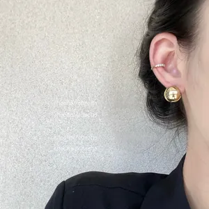 Détail d'une boucle d'oreille sphérique en or poli et d'un faux piercing serti de zircons