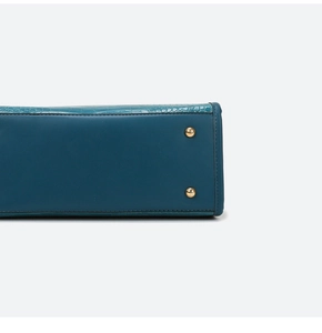 Close-up of bag bottom with protective gold metal feet and dark teal crocodile texture