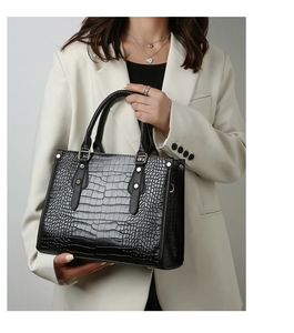Detail of black crocodile embossed leather handbag with gold rivets held by a model