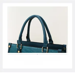 Close-up of deep teal crocodile embossed handbag with golden hardware and cylindrical handles
