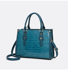 Detail of teal crocodile embossed tote bag with gold hardware and top handles