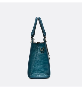 Detail view of teal crocodile texture leather handbag with gold-tone hardware and handle
