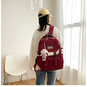 Detail of burgundy waterproof nylon backpack with white straps and plush rabbit charm