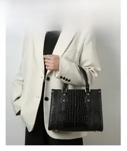 Classic black crocodile pattern handbag with gold rivets worn by model in white suit