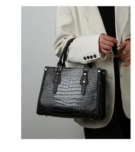 Detail of black crocodile pattern tote bag with gold rivets and handle on white suit