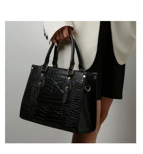 Detail of black crocodile pattern handbag with gold hardware held by a model