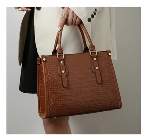 Detailed view of brown crocodile embossed handbag with gold rivets and double handles