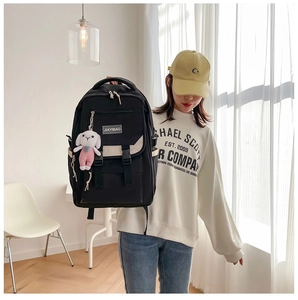 Close-up of black nylon backpack featuring a white rabbit plush charm and buckle closure