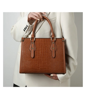 Detail of brown crocodile pattern handbag with golden studs and smooth top handle