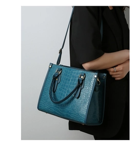 Detail of teal crocodile-patterned tote bag worn with black suit for business commute