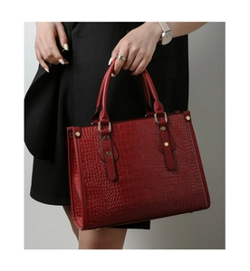 Detail of dark red crocodile embossed handbag with gold rivets held by a model
