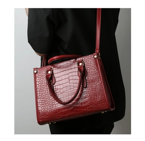 Detail of dark red crocodile embossed handbag with gold hardware and luxury leather texture