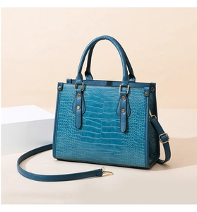 Detailed close-up of blue crocodile pattern handbag with gold rivets and detachable strap
