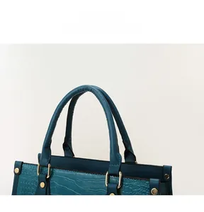 Close-up of teal faux-crocodile skin texture and gold hardware on luxury handbag