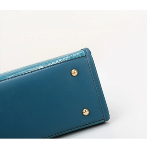 Detail of teal crocodile embossed leather bag with gold protective metal feet and fine stitching