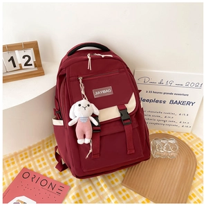 Detail view of burgundy nylon backpack with white straps and cute plush bunny charm