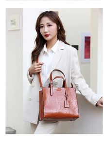 Detailed view of brown leather tote bag featuring embossed logo and metal bottom studs