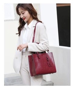 Detail of burgundy embossed leather tote bag with shoulder strap worn by a model