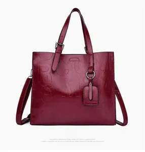 Close-up of embossed letter texture on dark red faux leather tote with shoulder strap