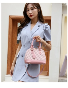 Pink shell handbag with geometric pattern held by a model wearing a light blue dress