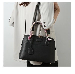 Detail of black lychee grain leather dome bag with decorative floral silk scarf handle