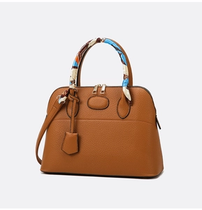 Detail view of caramel brown lychee leather handbag with decorative silk scarf on handle