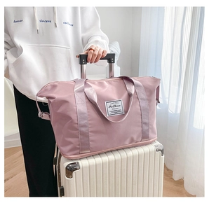 Pink travel duffel bag with bottom expansion compartment placed on a white suitcase