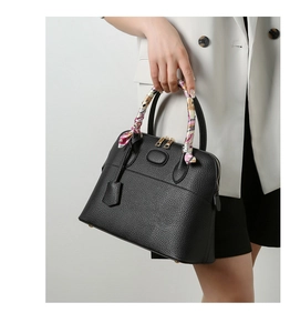 Close-up of black litchi leather tote bag with gold hardware and pink silk scarf handle