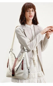 Détail de la sangle en cuir rouge avec des clous sur un sac blanc à motif litchi