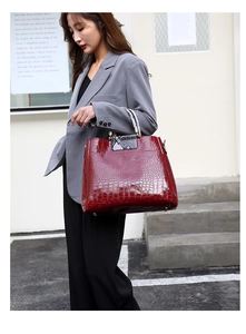 Detail of burgundy crocodile-embossed tote bag with snake print handles and gold hardware