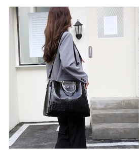 Detail of black crocodile embossed tote bag with chain handle on a model in sunlight