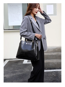 Detail of black croc-embossed handbag with gold hardware styled on a grey suit jacket