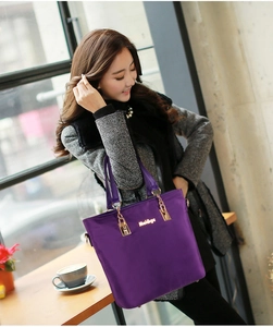 Detail of purple nylon tote bag featuring gold hardware and logo in a cafe setting