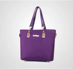 Detail of a purple nylon tote bag featuring a gold chain strap and metal logo plaque