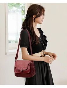 Detail of burgundy soft leather shoulder bag with round metal buckle on a model