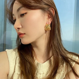 Detail of chunky gold irregular crinkled metal hoop earring on model for luxury fashion look