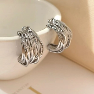 Silver twisted C-shape hoop earrings with multi-layered metal wire design on a white cup