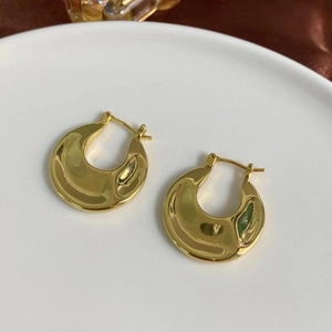 Macro shot of thick gold crescent hoop earrings with a polished mirror finish on white tray