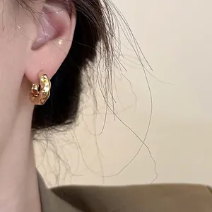 Fashionable golden geometric hoop earrings with textured hammered finish on female model