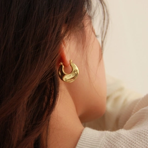 Detailed close-up of thick gold hoop earrings with a textured wavy metallic finish