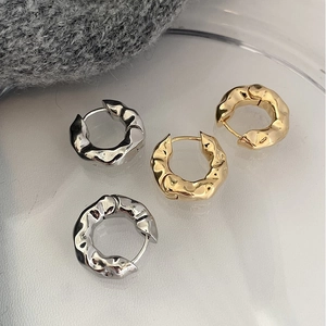 Detail of textured metal hoop earrings in gold and silver finish on a glass tray