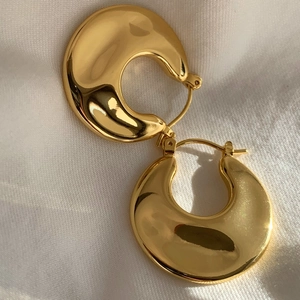 Detailed shot of golden textured hoop earrings with a glossy finish on white fabric