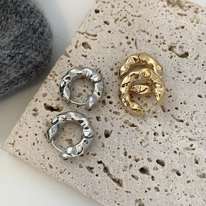 Macro detail of textured geometric gold and silver hoop earrings on a stone surface