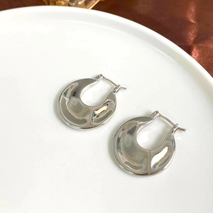 Detailed top view of silver C-shaped textured earrings on a white plate with satin fabric