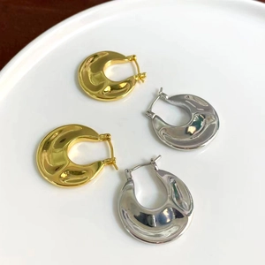 Detailed view of polished gold and silver textured hoop earrings on a white ceramic tray