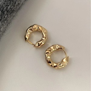 Macro detail of golden hoop earrings featuring irregular hammered texture and secure clasp