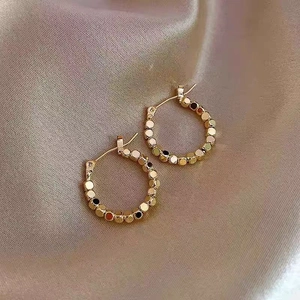 Detail of gold beaded hoop earrings featuring faceted metal beads on champagne silk