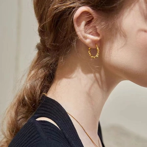 Close-up of golden hoop earrings with textured dotted surface on model's ear