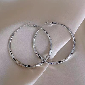 Polished silver metal hoop earrings with a twisted design on luxury silk fabric background